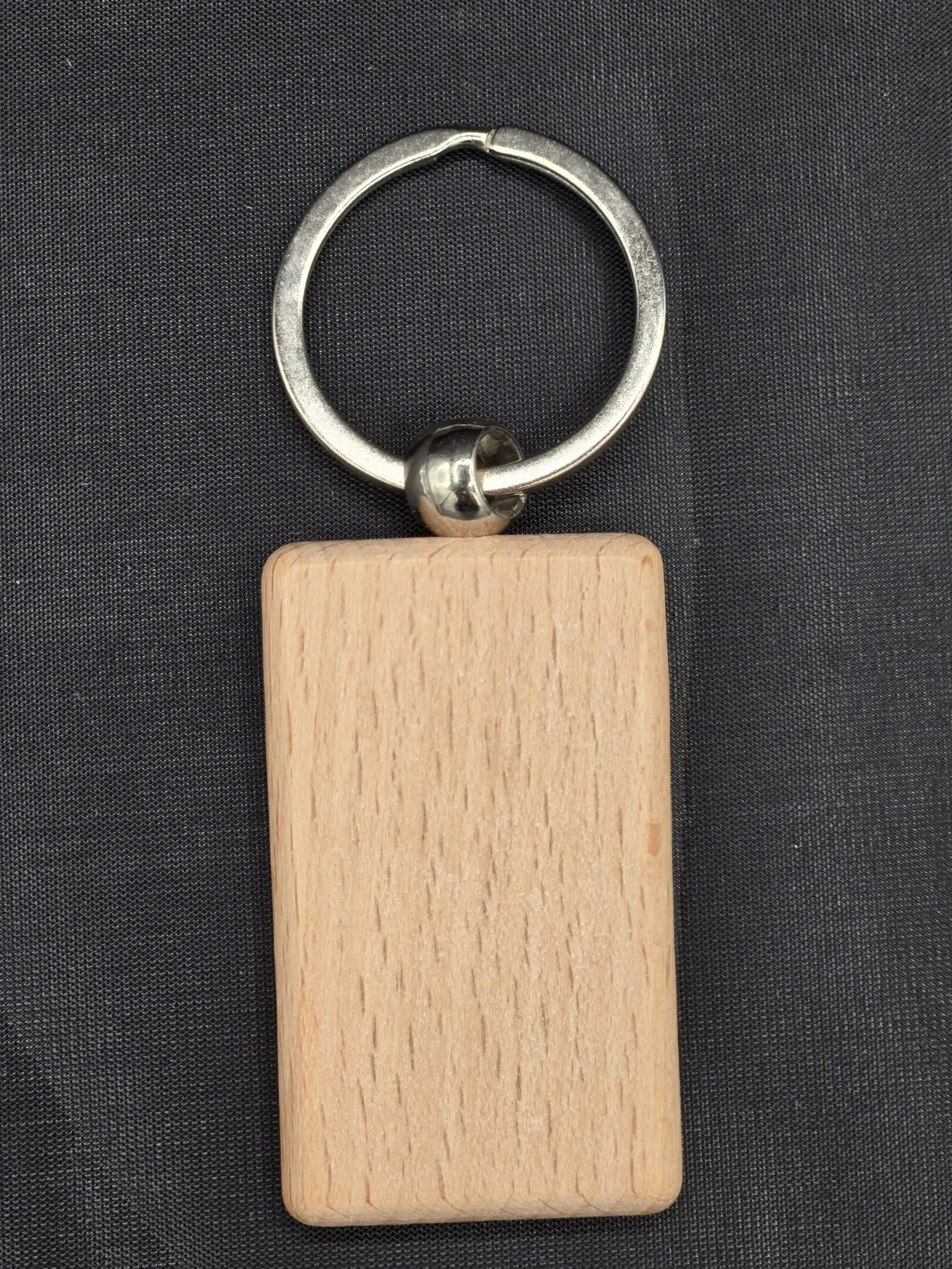 A rectangular wooden keychain with a metal ring on a black background.
