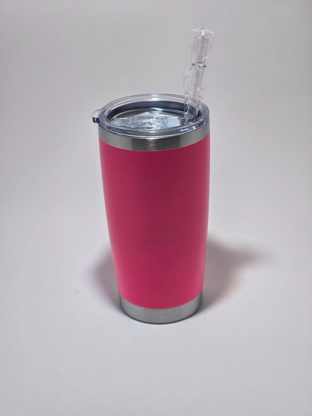 A pink insulated tumbler with a clear lid and straw on a white surface.