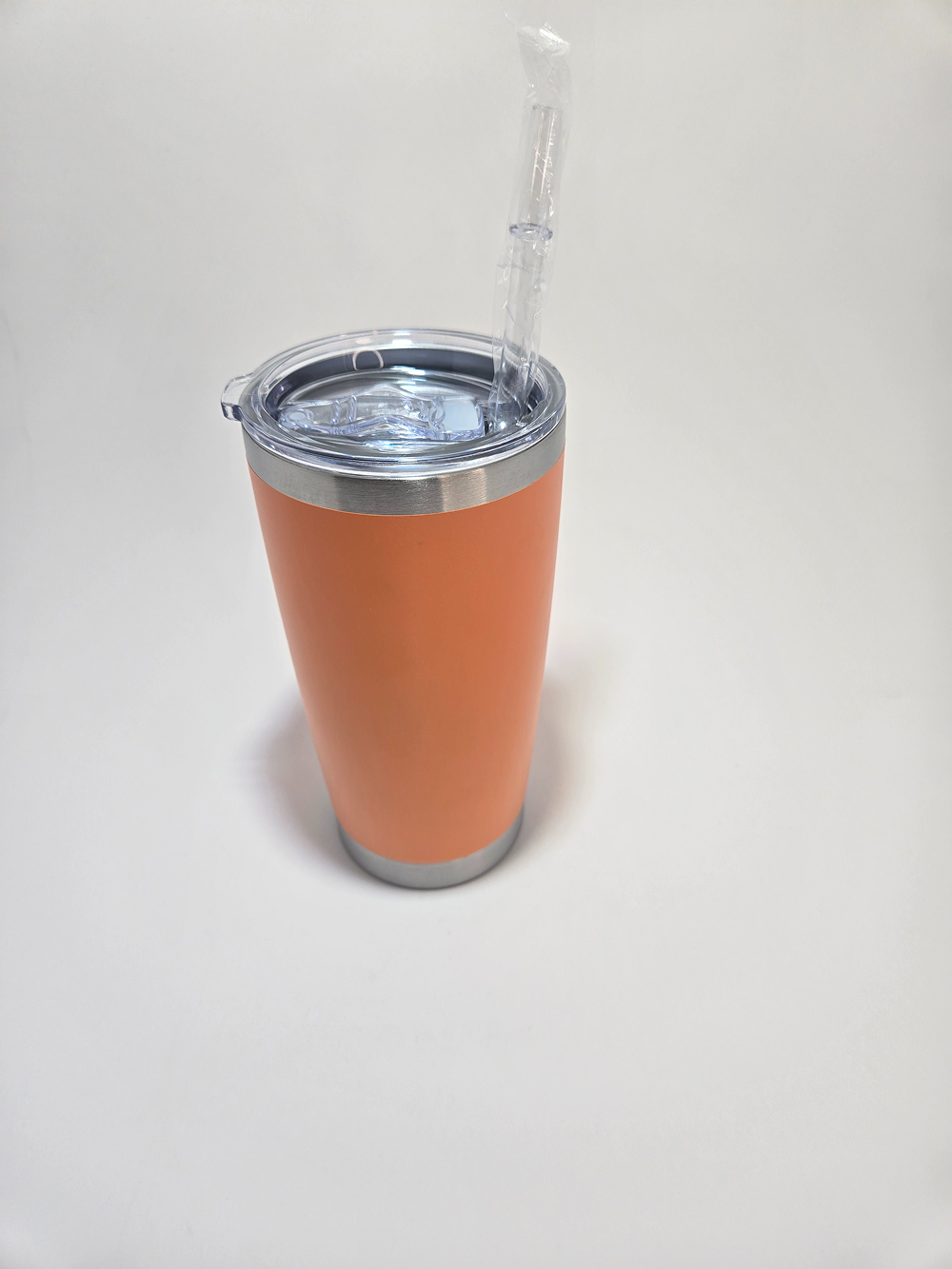 Orange insulated tumbler with clear lid on white surface.