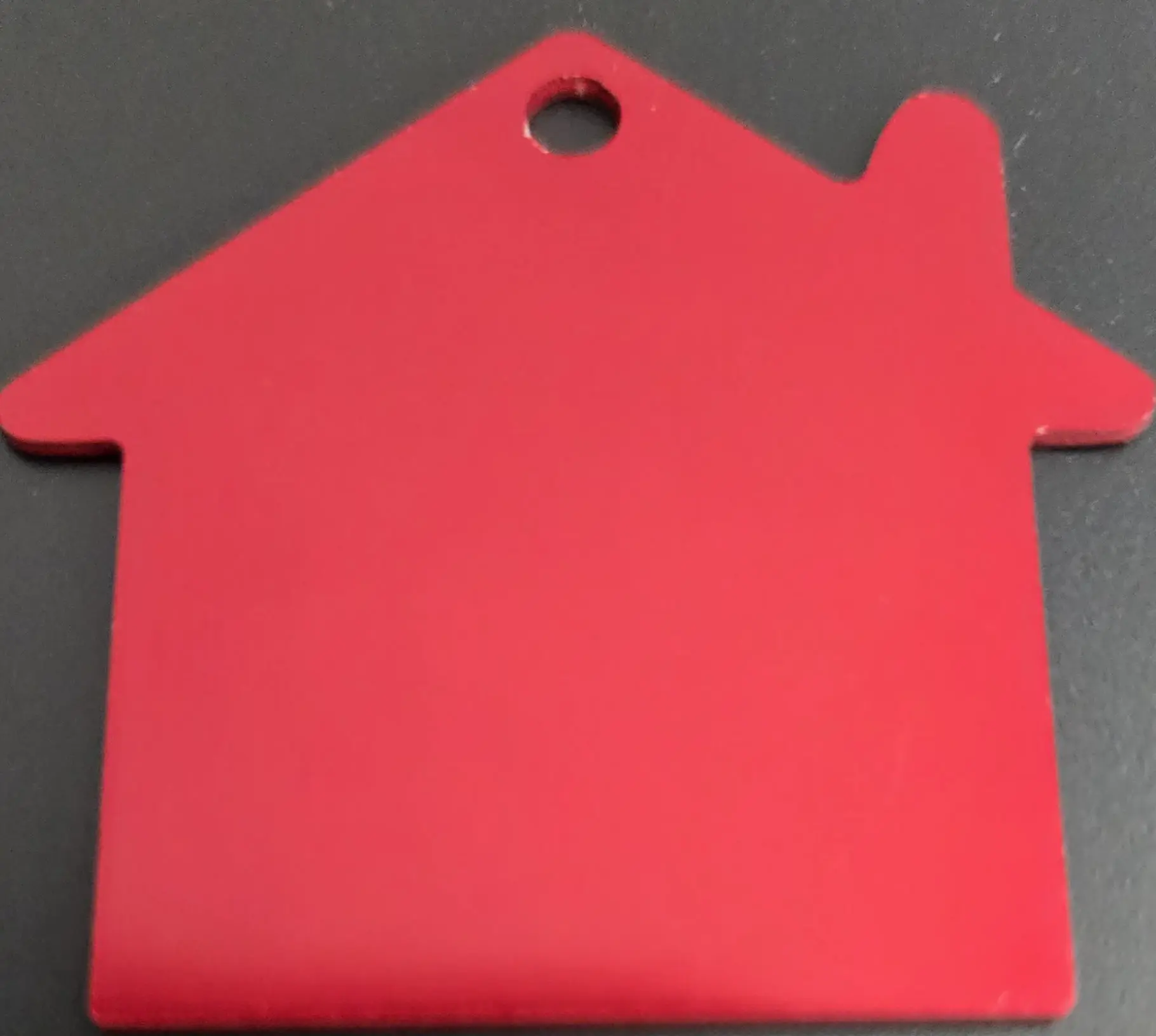 A red house-shaped object with a hole in the top corner on a dark surface.