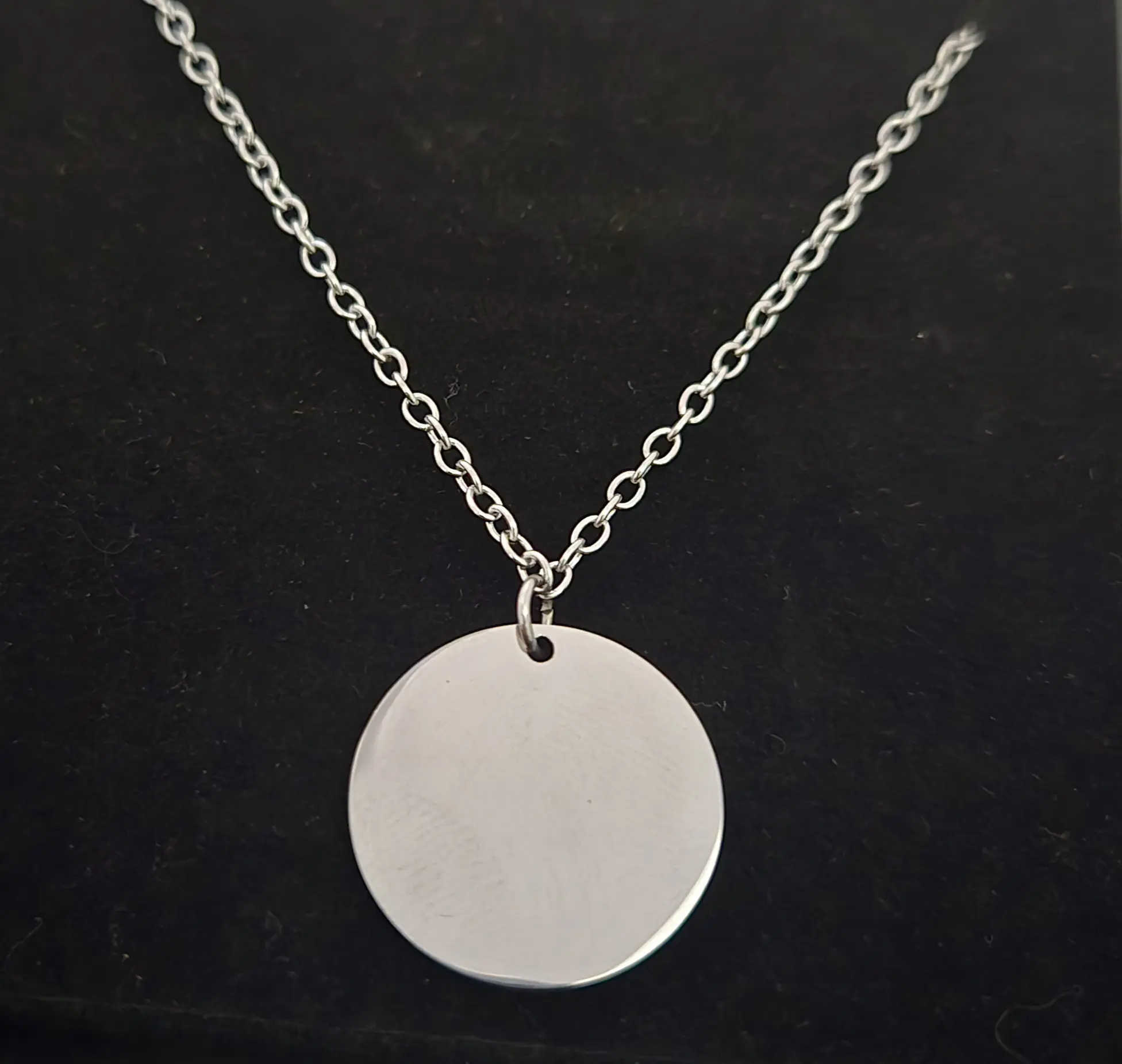 Silver necklace with a round blank pendant on a black background.