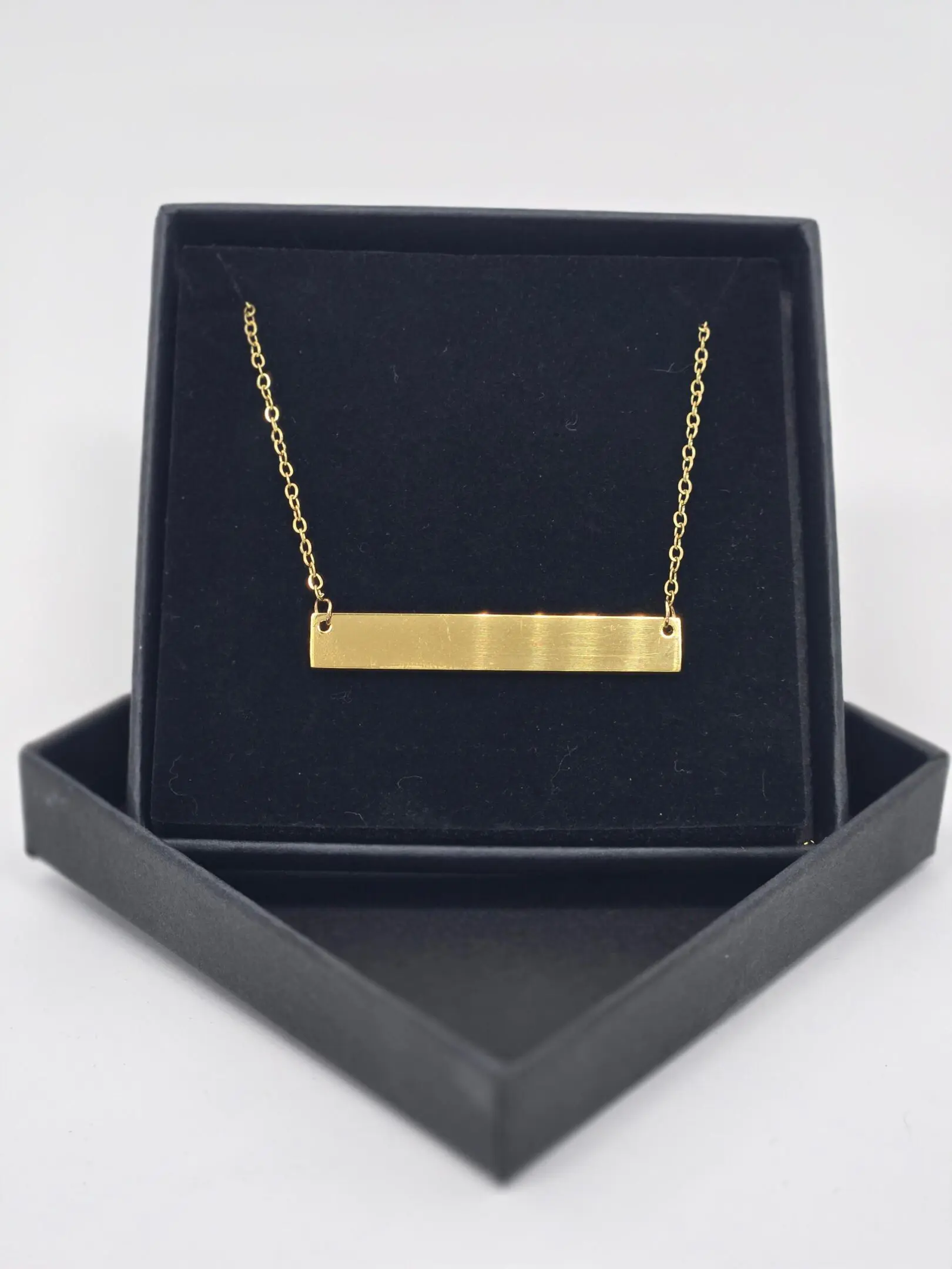 Gold bar necklace displayed in a black box.