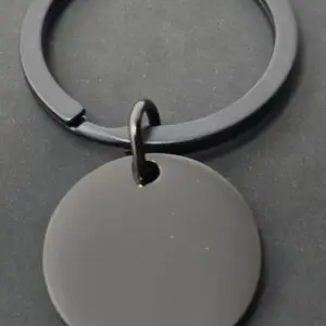 A black keychain with a round, blank pendant on a dark surface.