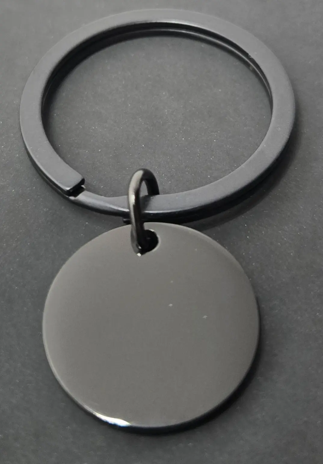 A black keychain with a round, blank pendant on a dark surface.