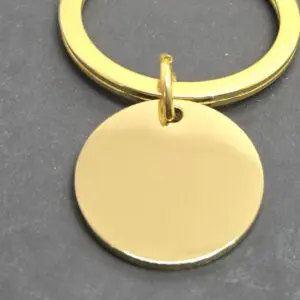 A shiny gold keychain with a round blank pendant on a gray surface.