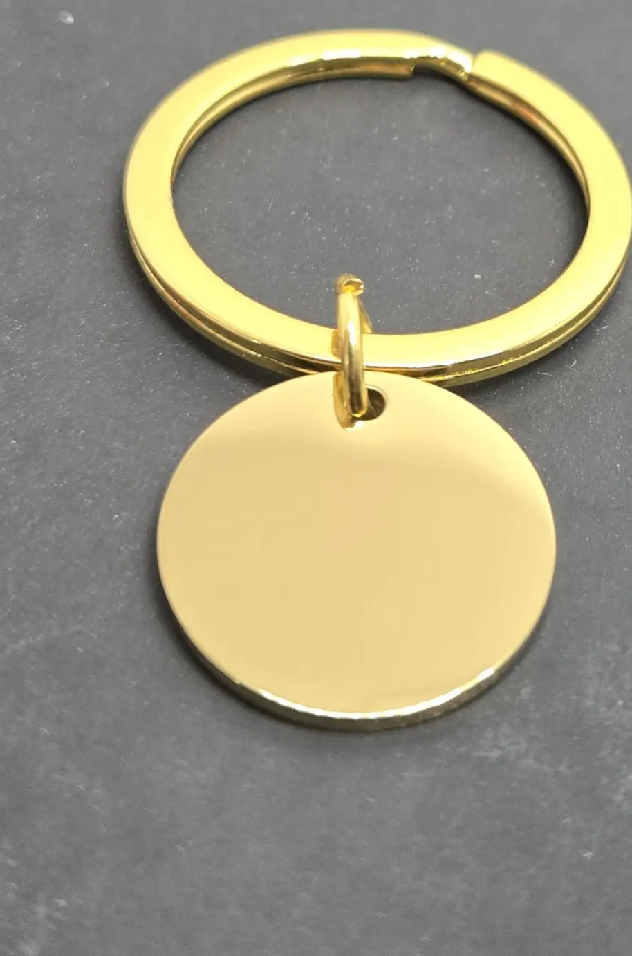 A shiny gold keychain with a round blank pendant on a gray surface.