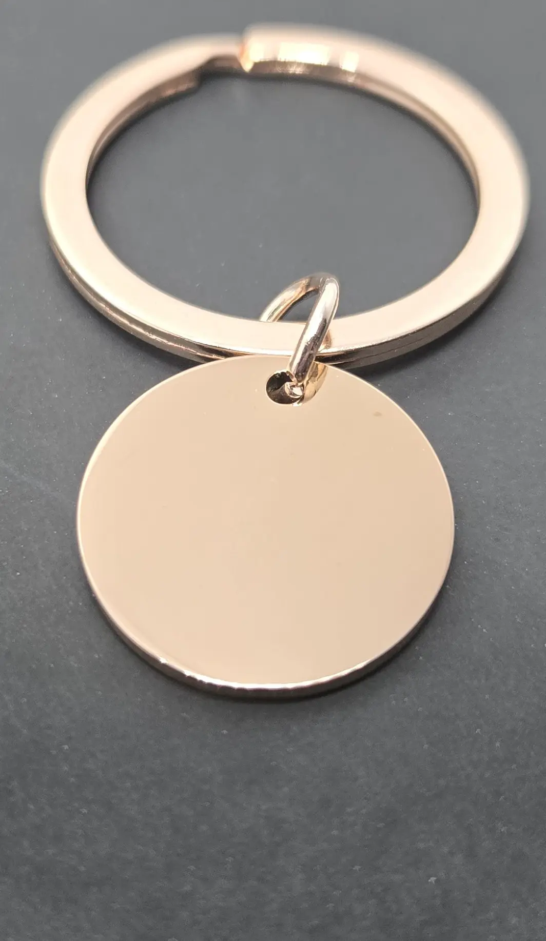 Close-up of a blank round metal keychain on a dark surface.