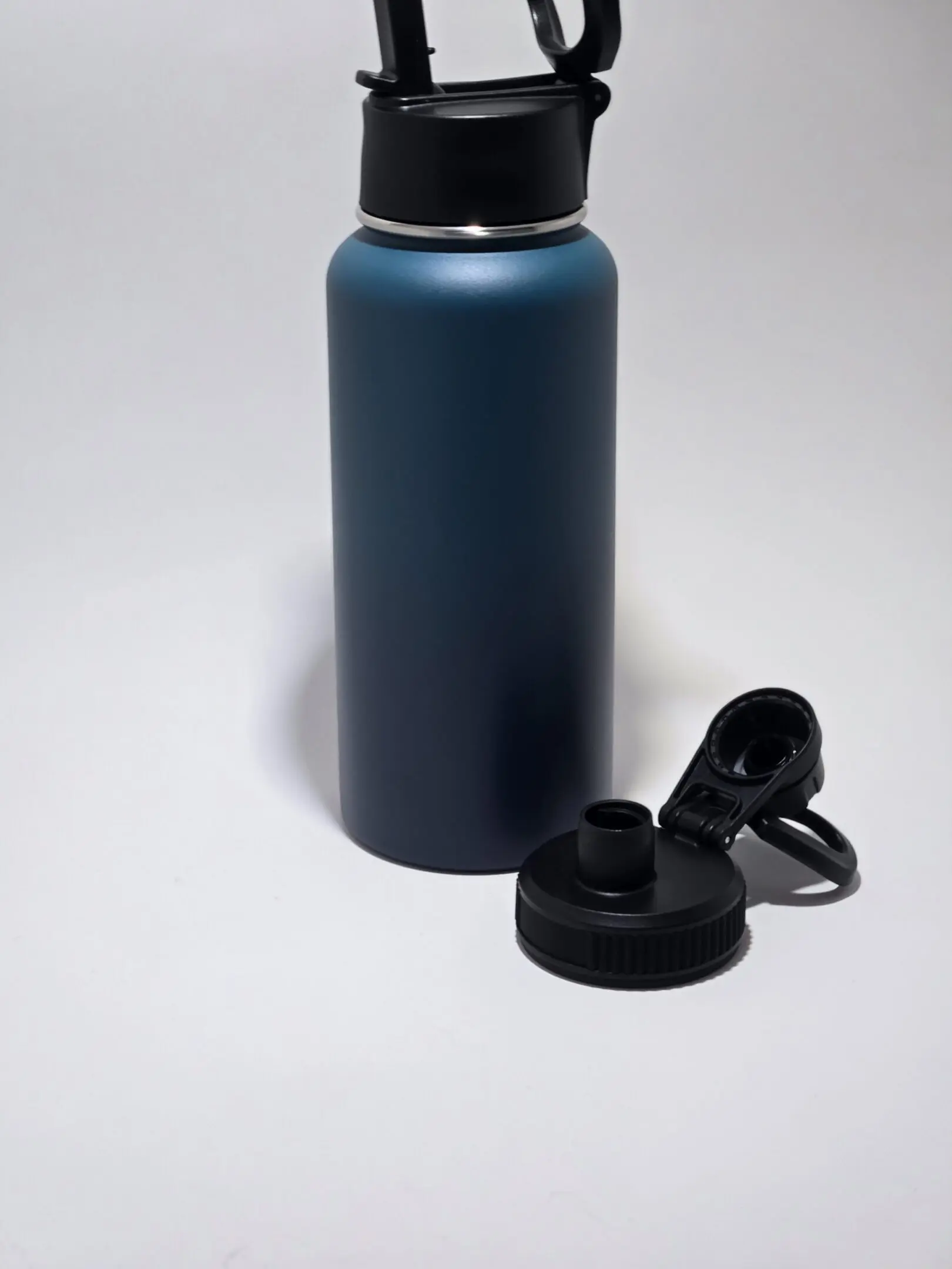 Blue insulated water bottle with a detachable black lid on a white surface.