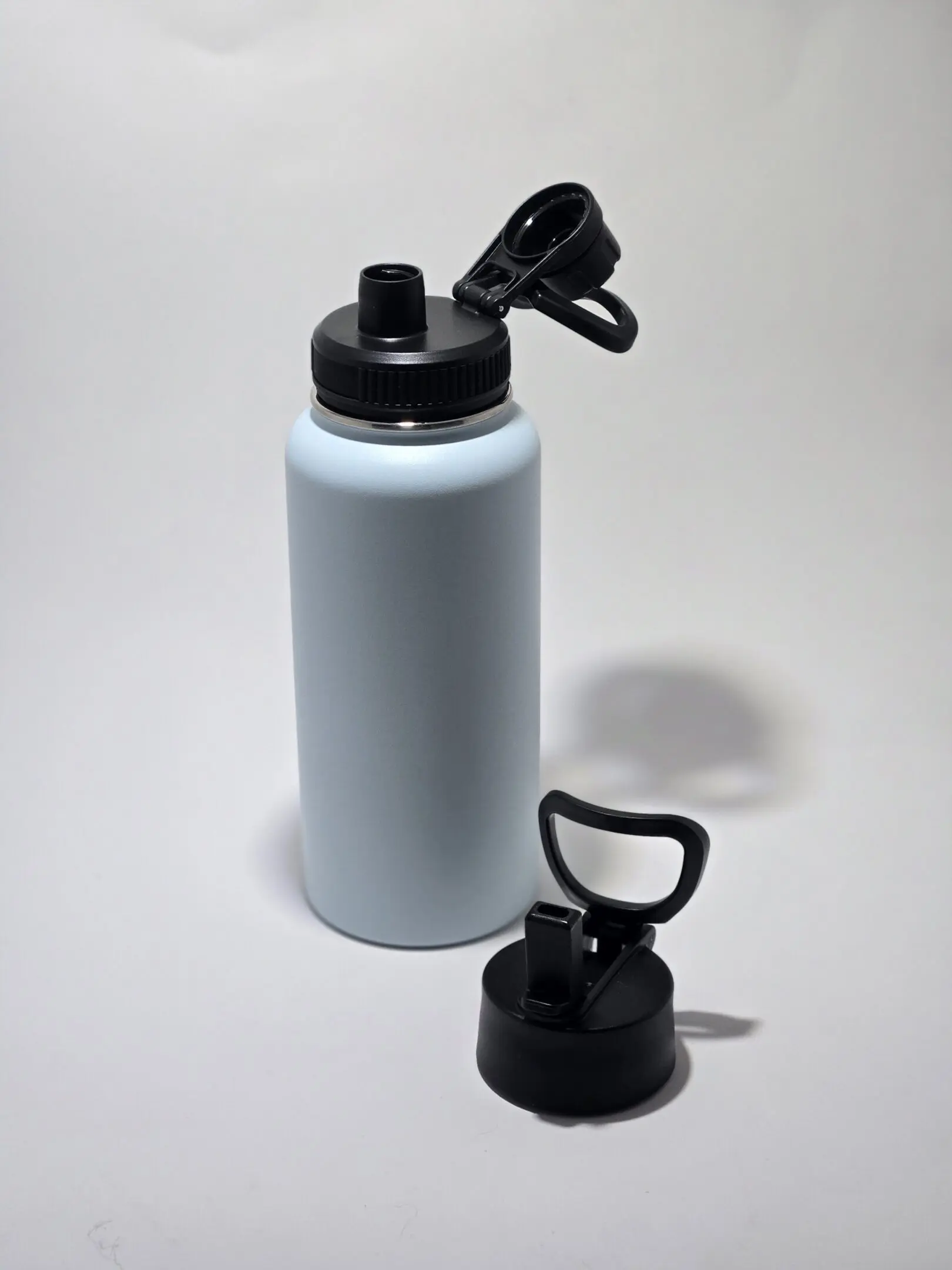 A white reusable water bottle with a black flip-top lid and a separate black handle lid.