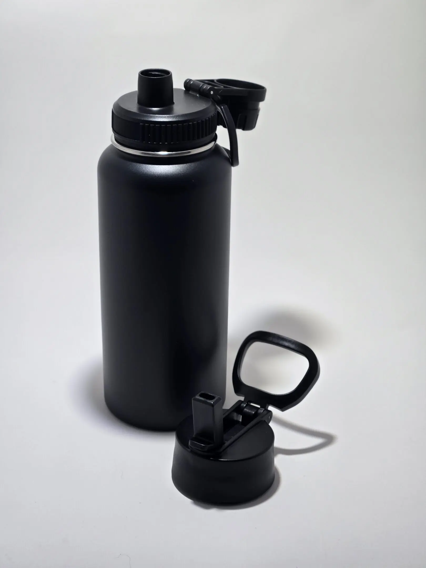 Black insulated water bottle with a detachable flip-top lid on a white surface.