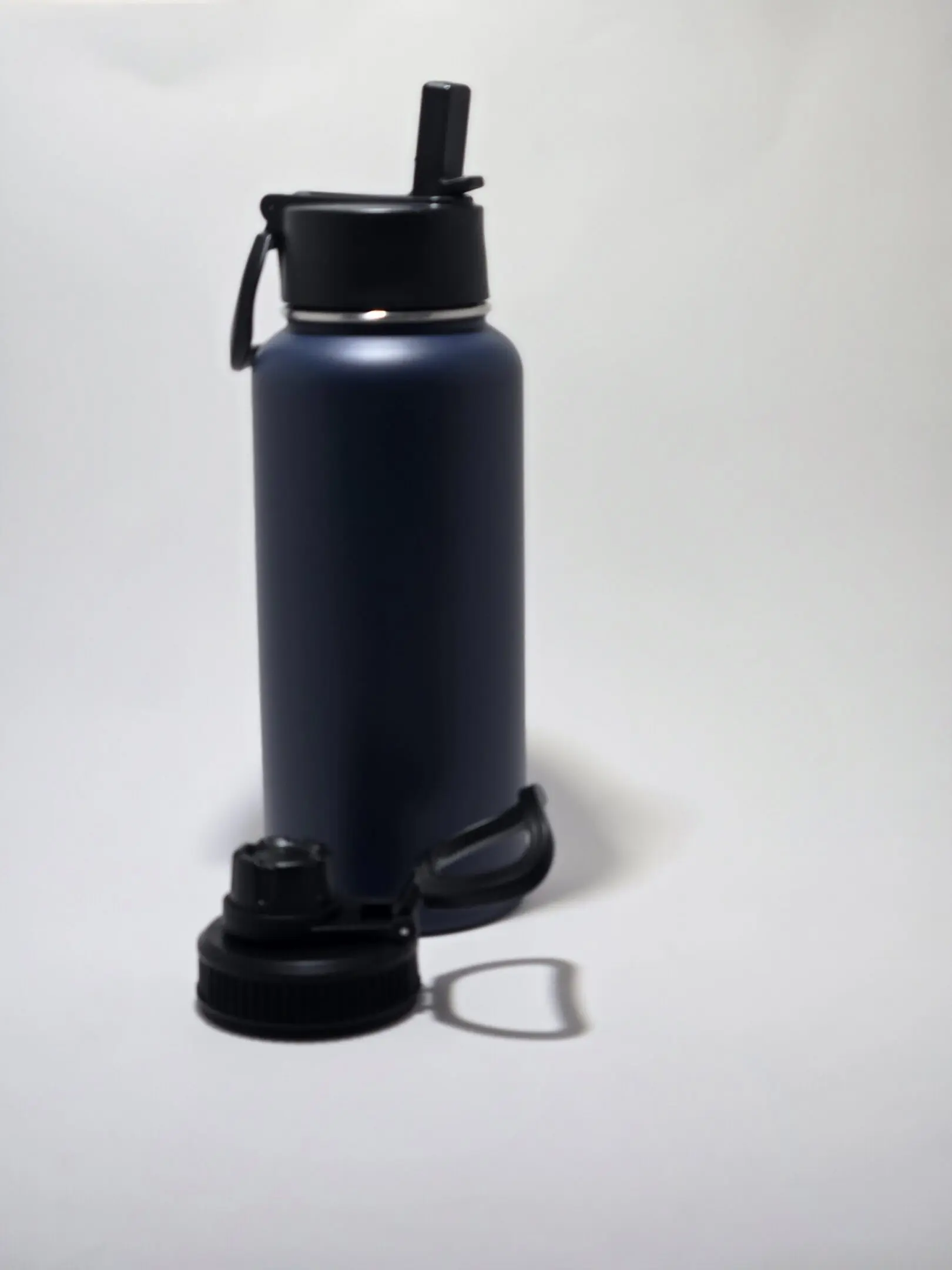 Navy blue water bottle with a black lid on a white surface.