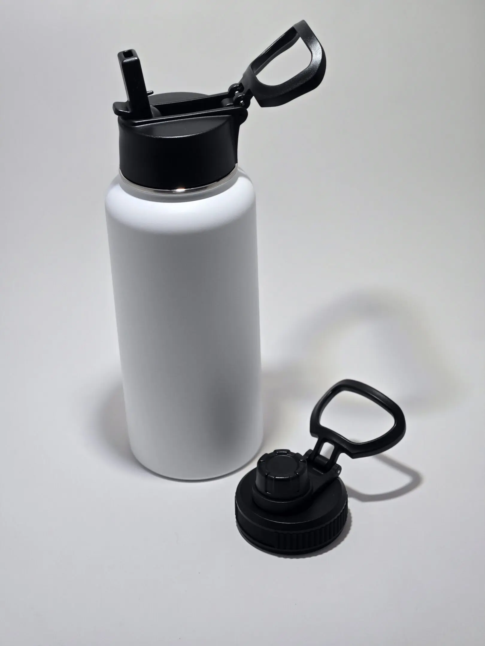 A white water bottle with a detachable black lid on a white surface.