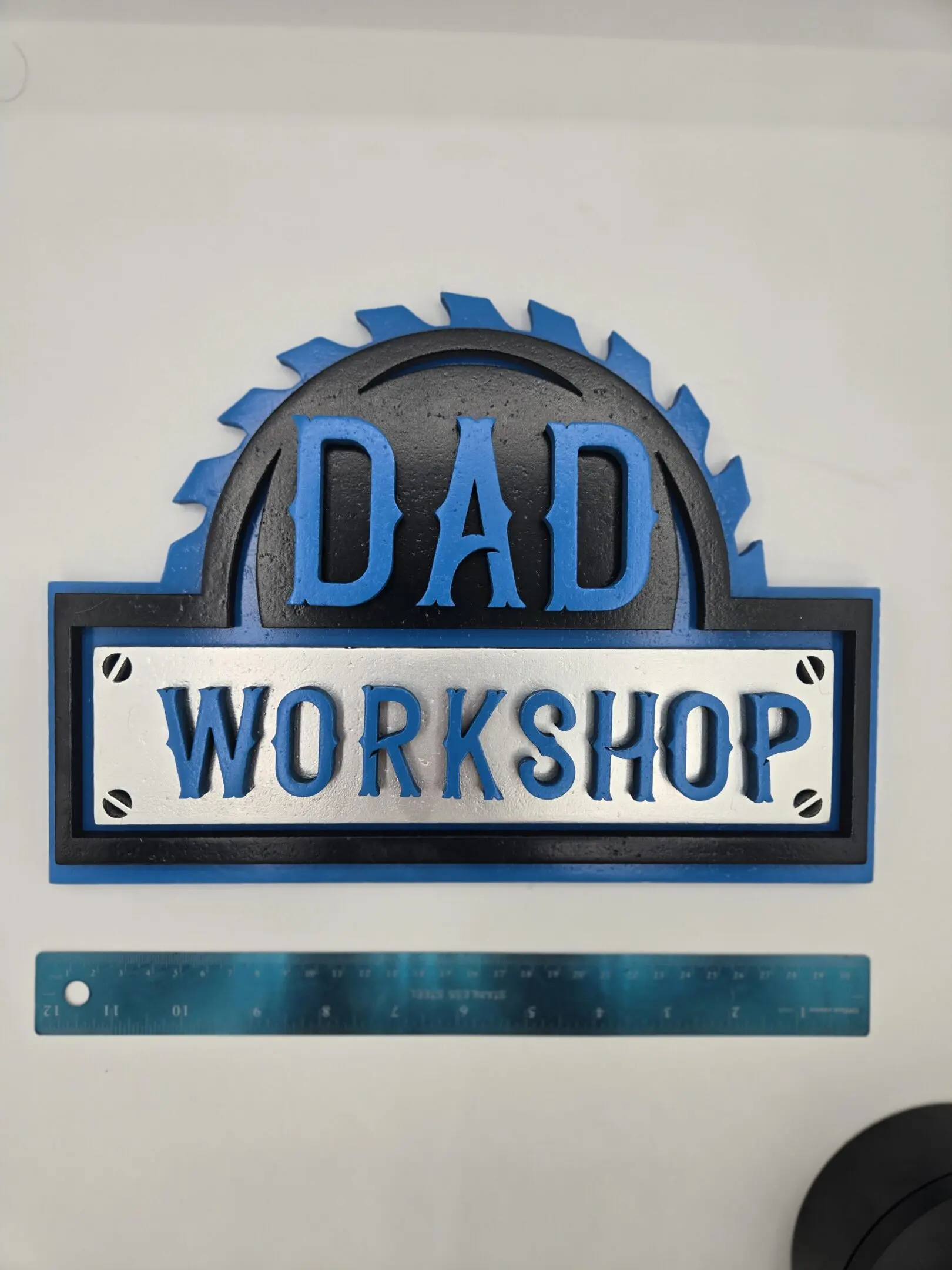 A blue and black sign saying 'DAD WORKSHOP' above a ruler.
